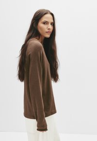 Brun langærmet top i blødt stof med en afslappet pasform og rund halsudskæring, kombineret med lyse, vidde bukser.