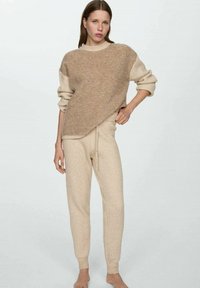 Beiges gestricktes Loungewear-Set mit einem weichen Pullover mit strukturiertem Oberteil und enganliegenden Ripp-Hosen. Die Zusammensetzung beinhaltet Wolle.