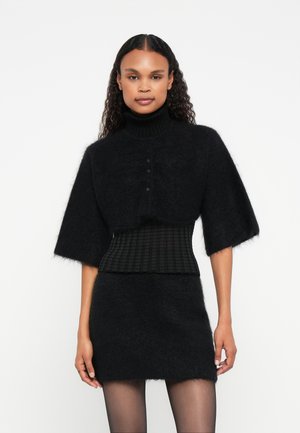 Sweater oversized preto com mangas curtas, gola alta canelada, fecho de botão e cintura ajustada texturizada; material suave e felpudo.