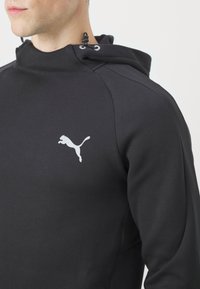 Sweat-shirt noir à capuche, avec un logo Puma blanc sur la poitrine. Le matériau est lisse avec des accents texturés sur les manches.
