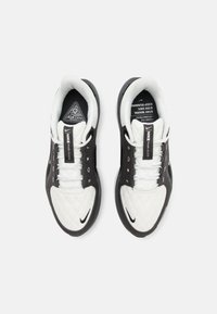 Zapatillas deportivas en blanco y negro con una punta blanca acolchada, lados de malla y acentos negros contrastantes. Presentan una suela redondeada y cordones.