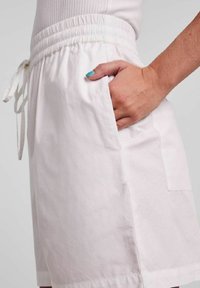 Bílé šortky z lehké látky, s elastickým pasem na stahovací šňůrku, bočními kapsami a volným střihem.