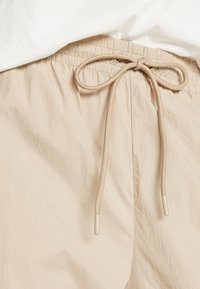 Lichtbeige shorts gemaakt van een geweven, lichtgewicht stof met een elastische tailleband en een trekkoord met zachte, ronde uiteinden.