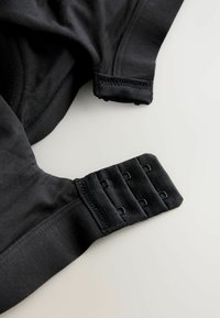 Schwarzes Stoffkleidungsstück mit einem Haken- und Ösenverschluss, der verstellbare Schlaufen bietet. Glatte Textur mit elastischen Kanten und genähten Nähten.