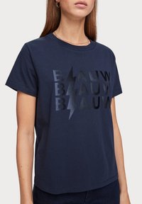 Camiseta de algodón azul marino con cuello redondo, con un diseño de rayo negro brillante y el texto "BLAUW" repetido. Mangas cortas.