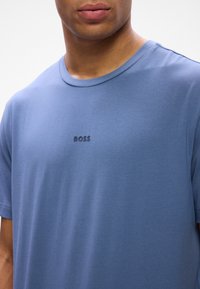 Zila kokvilnas T-kreklā ar apaļu kaklu, centrā ir neliels melns "BOSS" logo. Gluda tekstūra un īsas piedurknes.