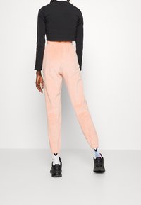 Rosa kordflorbyxor med elastiska muddar, i kombination med en svart kortärmad långärmad topp. Skorna är svarta sneakers och mönstrade strumpor.