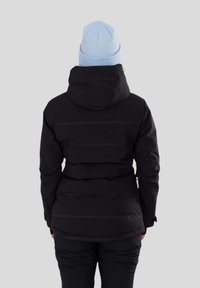 Czarna kurtka puchowa z kapturem i poziomymi detalami szwów. Noszona na ciemnych spodniach, w zestawie z jasnoniebieską dzianinową czapką.