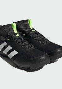 Baskets de sport noires avec une tige texturée, trois bandes blanches et des accents vert fluo sur le col et les lacets. Semelle en caoutchouc avec des crampons.