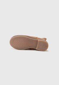 Pantof cu talpă de piele maro cu vârful rotunjit și suprafața netedă. Tălpicul din cauciuc texturat cu un model mic de stele pentru tracțiune.