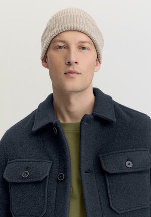 Dunkelblaue Wolljacke mit zwei knöpfbaren Taschen, kombiniert mit einer hellbeigen gerippten Mütze und einer grünen Innenlage. Schlichtes, strukturiertes Design.