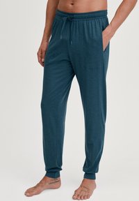 Turquoise loungebroeken gemaakt van zachte stof, met een elastische tailleband, een trekkoord, zijzakken en taps toelopende manchetten.