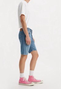 Jeansshorts i ljusblått, medelhöga till låren, med framfickor och en brun läderlapp. Matchas med vit t-shirt och rosa högklackade sneakers.