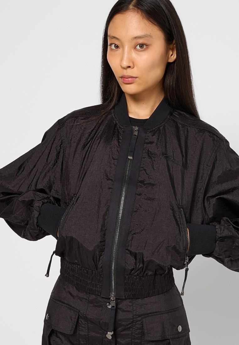 Schwarze Bomberjacke aus strukturiertem Stoff, mit Reißverschluss, gerippten Bündchen und elastischem Taillenbund. Minimalistisches Design ohne sichtbare Logos.