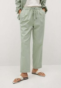 Světlé zelené, lehké kalhoty s elastickým pasem, bočními kapsami a zúženým střihem. Spárované s plochými sandály s otevřenou špičkou.