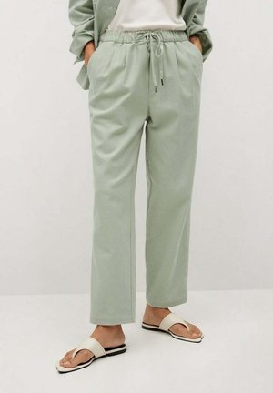 Lys grønne, lette bukser med elastisk talje, side lommer og tapered snit. Bærer flade, åbne sandaler.