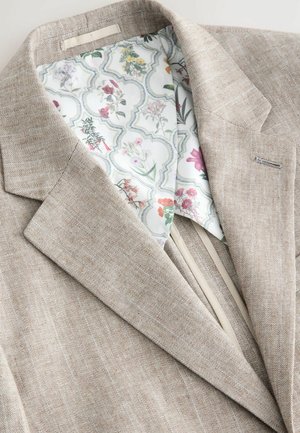Chaqueta de traje de lino beige con forro de estampado floral. Presenta un exterior texturizado y un corte moderno con solapas de pico.