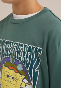 Groene katoenen t-shirt met een grafische print van een cartoonfiguur en tekst, ronde hals, korte mouwen en een losse pasvorm.