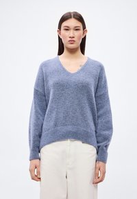 Μπλε πλεκτό πουλόβερ με V-λαιμόκοψη, χαλαρούς ώμους και ριμπ τελείωμα. Μαλακή υφή, άνετη εφαρμογή και μακριά μανίκια. Συνδυασμένο με ανοιχτόχρωμο παντελόνι.