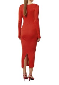 Rotes geripptes Strickkleid mit langen Ärmeln und einem Schlitz im Rücken, das eine figurschmeichelnde Silhouette zeigt. Kombiniert mit roten Absatzsandalen.