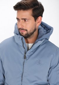 Lys blå polstret jakke med lynlås foran, justerbar hætte og ankre logo detail på brystet. Glat tekstur og holdbart stof.