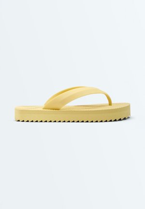 Sandale tongs en caoutchouc jaune avec semelle texturée et épaisse bande de roulement en zigzag, présentée en profil latéral sur un fond blanc uni.