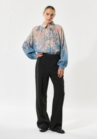 Lichtblauwe blouse met bloemenpatroon, voorzien van pofmouwen en een knopenlijst, gecombineerd met hoge zwarte broek met knoopaccenten.