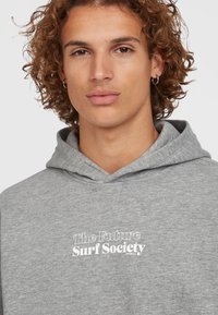 Grijze hoodie met een kangoeroezak, voorzien van witte tekst "The Future Surf Society." Zacht materiaal en een standaard pasvorm met een capuchon met trekkoord.