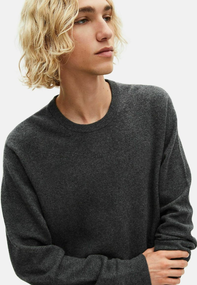 Donkergrijze crewneck trui gemaakt van zachte breigoedstof. Heeft een geribbelde halslijn en manchetten. Eenvoudig ontwerp zonder zichtbare patronen of accenten.