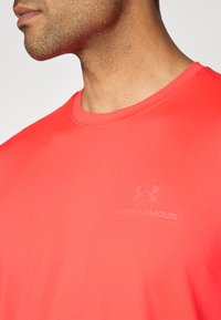 Rød trenings T-skjorte laget av glatt stoff. Har rund hals og et svakt trykt logo på brystet.