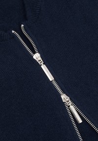 Granatowy sweter z zamkiem błyskawicznym wykonany z teksturowanego dzianiny, z srebrnym zamkiem z logowanym uchwytem i prążkowanym kołnierzem, podkreślający czysty, nowoczesny design.