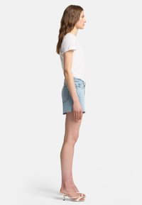 Ljusblå denimshorts med fransad nederkant, i kombination med en enkel vit t-shirt och beige remsandaler med hög klack.