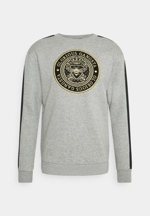 Felpa grigia a maniche lunghe con righe nere sulle maniche e un emblema rotondo nero e oro che presenta un'ape e la scritta "Glorious Gangsta" sul petto.
