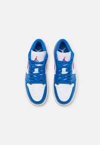 Baskets basses blanches et bleues avec un logo rouge, des lacets bleus et une zone perforée au niveau des orteils, vues de dessus sur un fond uni.