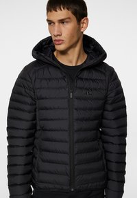 Svart puffjacka med quiltad design, huva, framdragkedja och sidofickor, med en slät yta och slim fit.