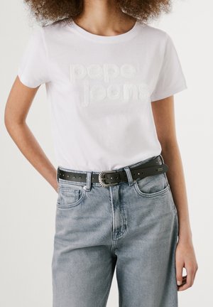 Osoba nosi białą koszulkę Pepe Jeans wpuszczoną w jasnoniebieskie, wysokiej talii dżinsy z czarnym paskiem i ozdobną klamrą.
