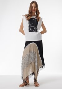 Top blanco sin mangas con un gráfico negro, combinado con una falda asimétrica plisada en beige, negro y detalles de encaje, completado con sandalias planas.