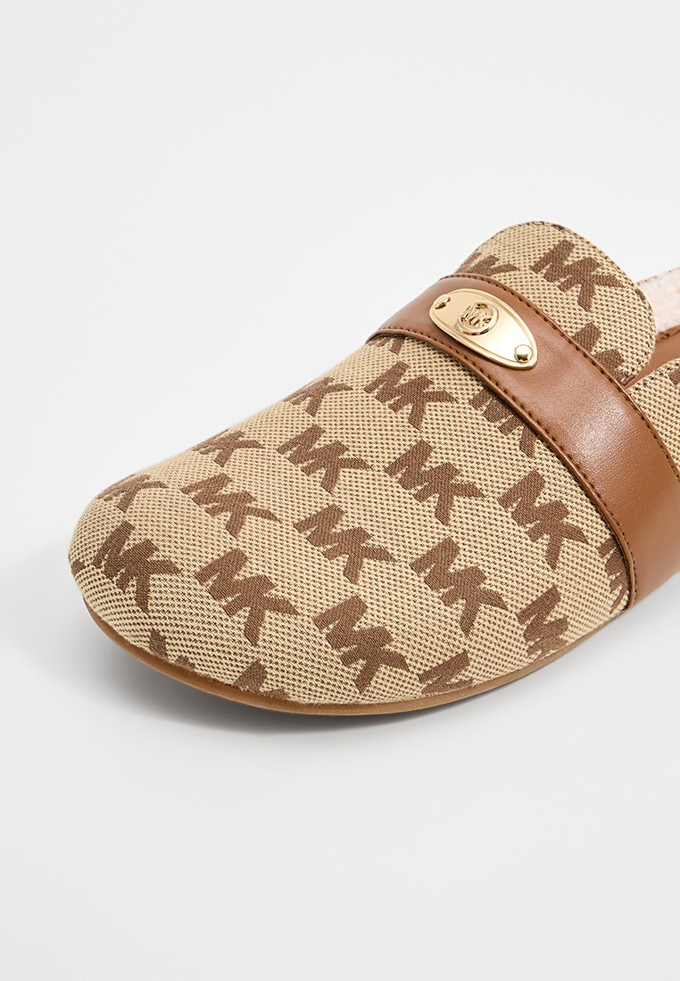 Slip-on sko med en beige canvas ovandel och ett brunt monogrammönster, bruna läderdetaljer och en guldfärgad logotyp.