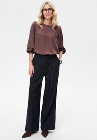 Brązowa satynowa bluzka z bufkami, zestawiona z czarnymi, szerokimi spodniami z wysokim stanem i paskiem do wiązania. Elegancki, dopasowany fason.