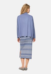 Hellblauer Pullover mit oversize Schnitt und langen Ärmeln, kombiniert mit einem bedruckten Midirock, der kreisförmige und gestreifte Muster aufweist. Graue flache Schuhe.
