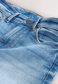 Niebieskie dżinsy z denimu z przednim guzikiem i szlufkami na pasek, pokazujące przednią kieszeń oraz pomarańczowe przeszycia na jasnym tle.
