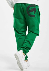 Grønne bomulds-sweatpants med en sort grafik på baglommen. Har elastiske manchetter og en afslappet pasform. Sættes sammen med hvide sneakers.