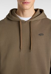 Brauner Hoodie aus Baumwollmischung, mit Kordelzug, gerippten Bündchen und einem kleinen dunklen Logo auf der Brust. Weicher Stoff, lockere Passform.