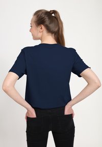 Námořnická modrá tričko s krátkým rukávem a kulatým výstřihem, zobrazené ze zadu. Tkanina vypadá hladce, bez viditelných vzorů či ozdob.