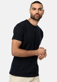 Schwarzes kurzärmliges T-Shirt mit rundem Halsausschnitt, das ein dezentes Streifenmuster in Blau und Weiß aufweist und eine kleine Brusttasche hat.