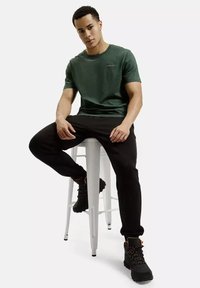 Ciemnozielona bawełniana koszulka z okrągłym dekoltem, w połączeniu z czarnymi tapered joggerami oraz wytrzymałymi czarnymi butami z pomarańczowymi akcentami.