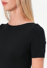Top nero a maniche corte con scollo rotondo, realizzato in tessuto liscio. La vestibilità è aderente al corpo, mettendo in risalto un design pulito.