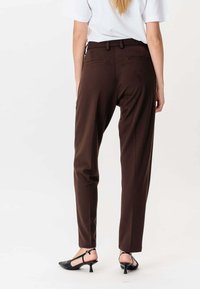 Hnědé kalhoty na míru se slim fit střihem, s zadními kapsami a hladkým povrchem. V kombinaci s černými lodičkami.