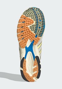 Εξωτερική σόλα παπουτσιού με λαστιχένιο σχέδιο σε πορτοκαλί και μπλε μοτίβα πρόσφυσης, υφασμένη με ανάγλυφες κουκκίδες και αυλακώσεις για καλύτερο κράτημα και ευελιξία.