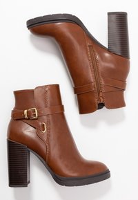 Hnědé kožené kotníkové boty s vysokým blokovým podpatkem, bočním zipem a ozdobným páskem se zlatou přezkou. Hladká textura a elegantní design.